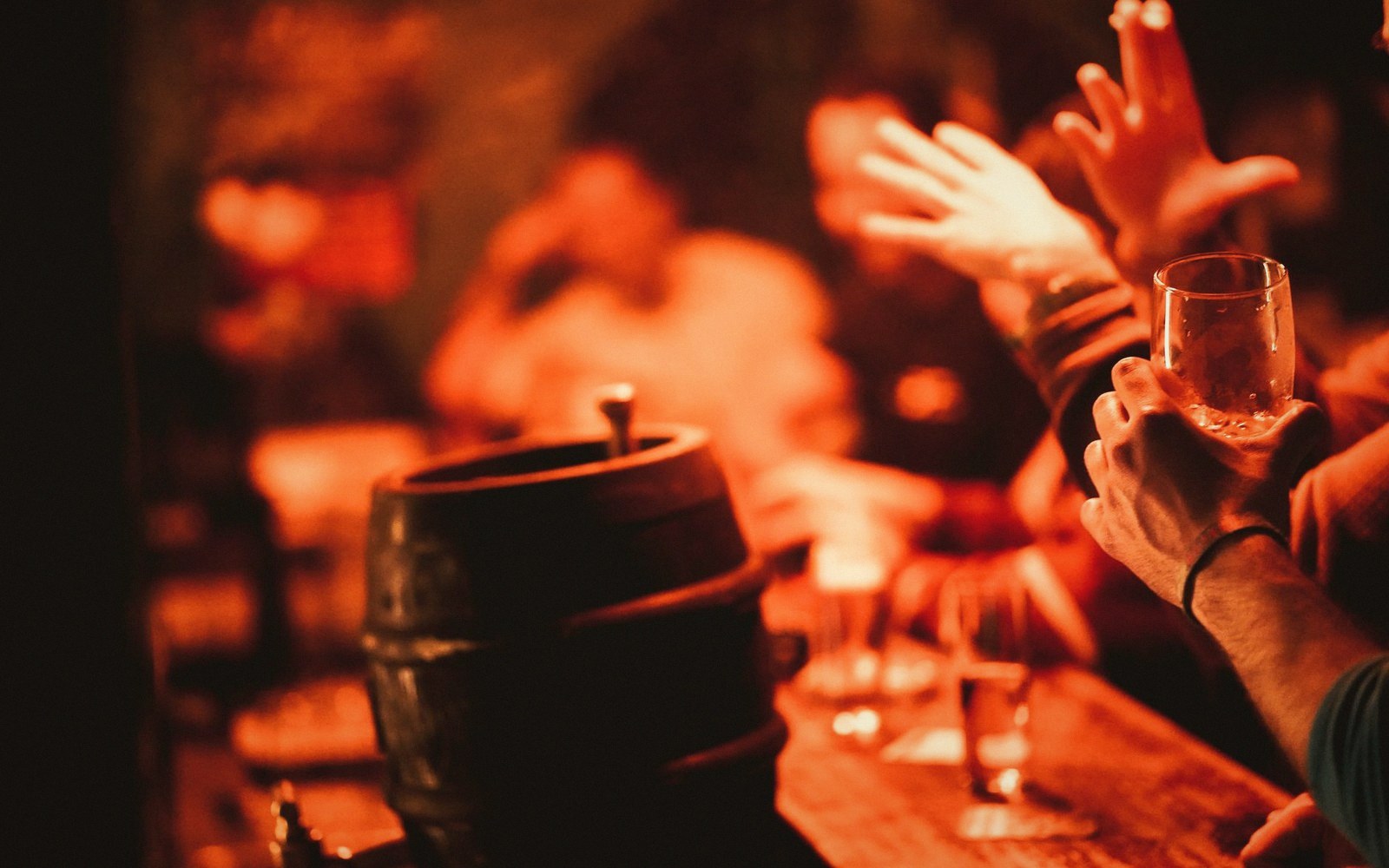 Hands raised near a wooden barrel and glasses in a dimly lit bar