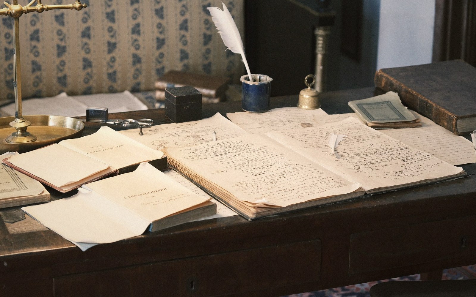 Handwritten manuscript pages and a quill pen laid out on an antique wooden desk