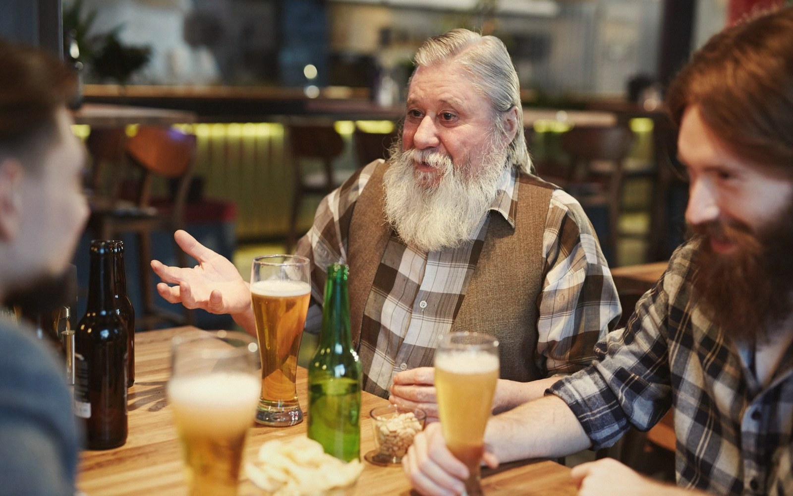 Bearded men chat over glasses and bottles of beer at a pub table