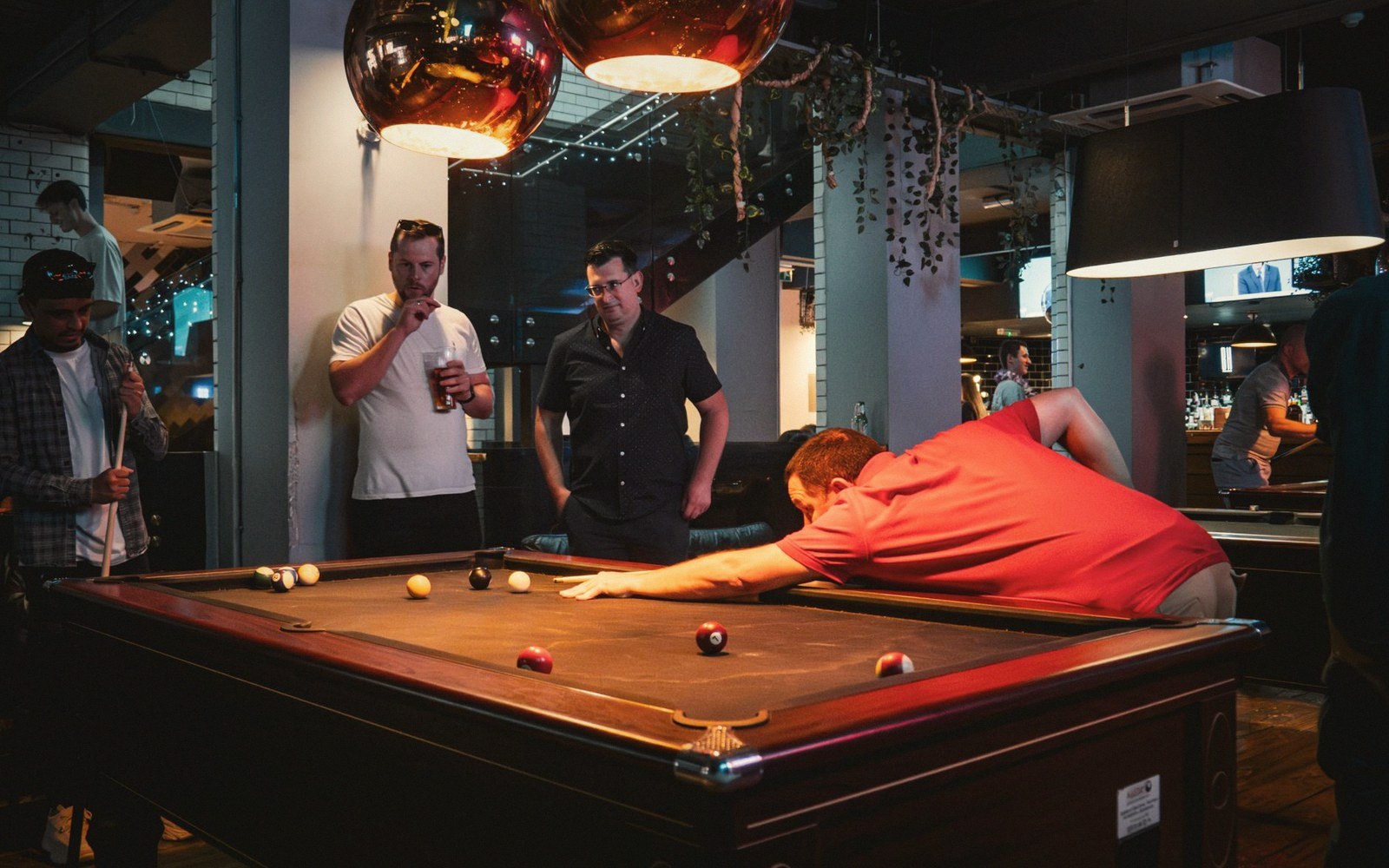 A man leans across a pool table to take a shot while friends watch