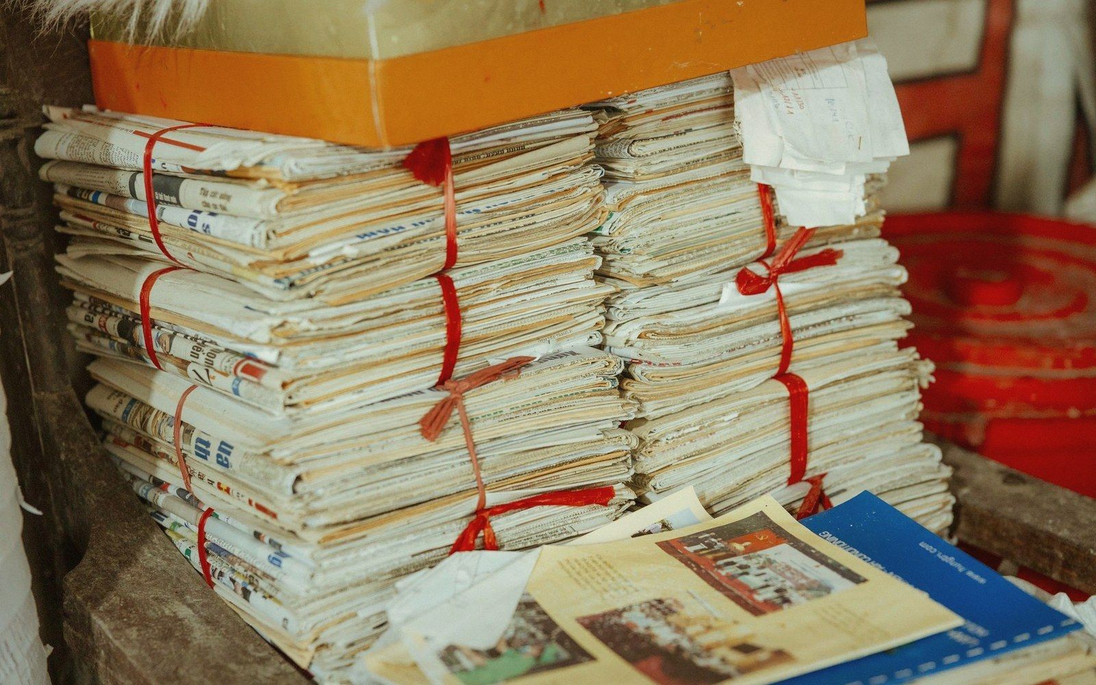Bundled stacks of old newspapers tied with red string beside an open magazine